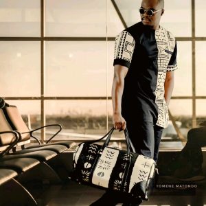 Homme portant une création TOMENE MATONDO avec sac afro-chic noir et blanc dans une ambiance lifestyle premium.